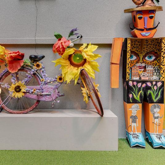 A bicycle decorated with flowers and a colourful artistic statue at the Atrium at ClinkNOORD Hostel in Amsterdam.