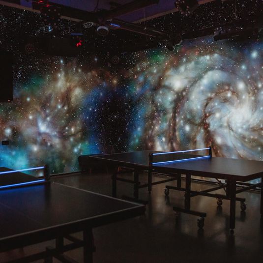 The Galaxy Room at ClinkNOORD hostel in Amsterdam with space-inspired murals on the walls and table tennis tables set up.
