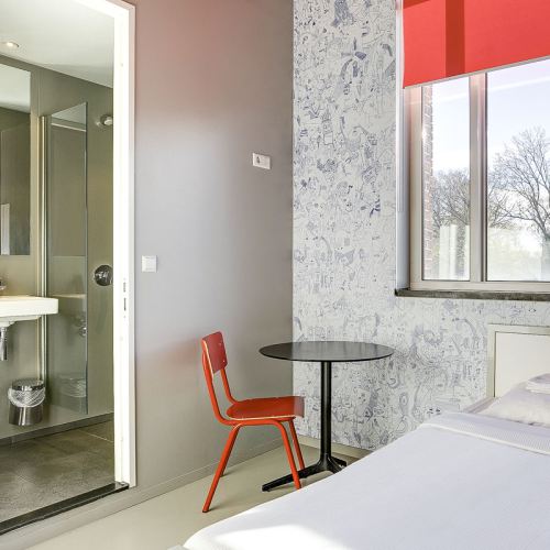 a private room at ClinkNOORD hostel in Amsterdam showing a double bed, a table and chair and a private bathroom