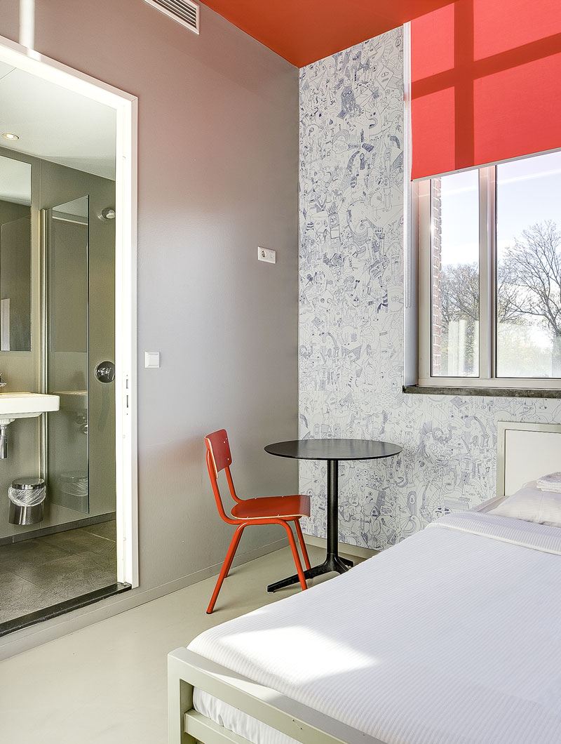 A private room at ClinkNOORD Hostel in Amsterdam with a double bed, chair, table, ensuite bathroom, decorated wallpaper and window.