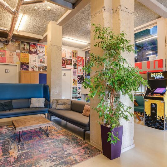 A social space in ClinkNOORD Hostel in Amsterdam with seating, plants and retro video games, where travellers can relax and meet eachother.