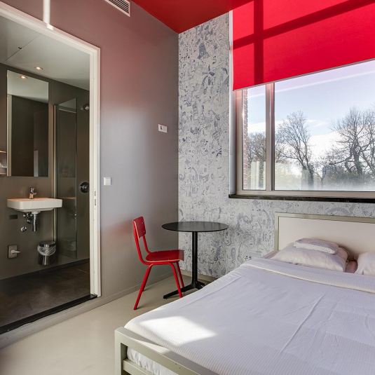 A private double room at ClinkNOORD hostel in Amsterdam with a double bed, table, chair and bathroom