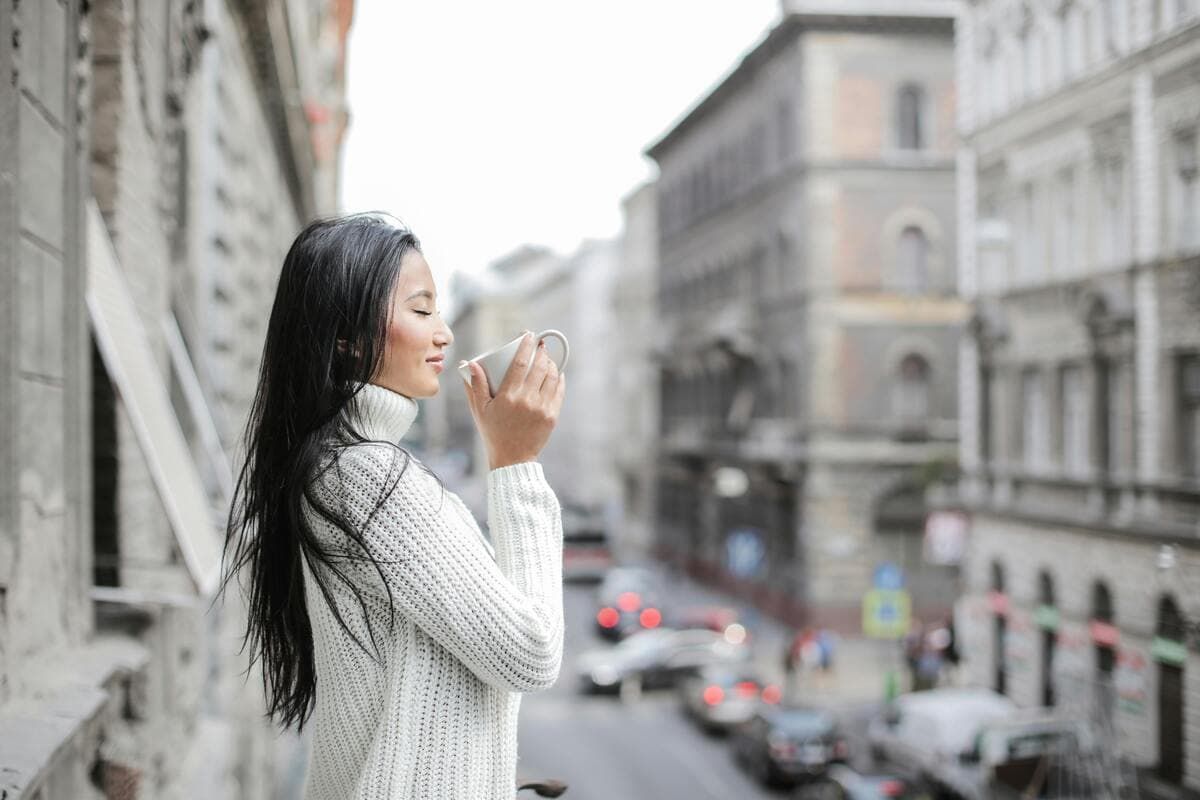Lady standing outside, drinking coffee.