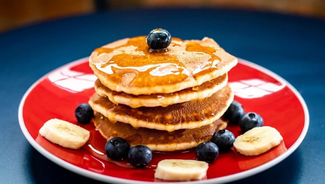 Pancakes with maple syrup drizzled on top with blueberries and banana slices on the plate