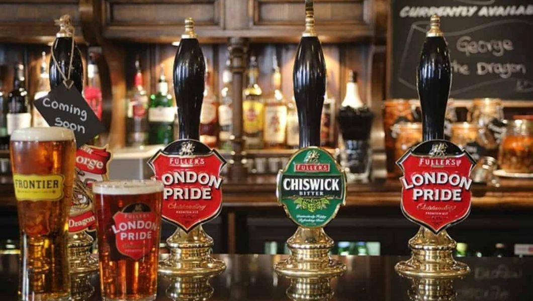 two glasses of beer in front of beer taps