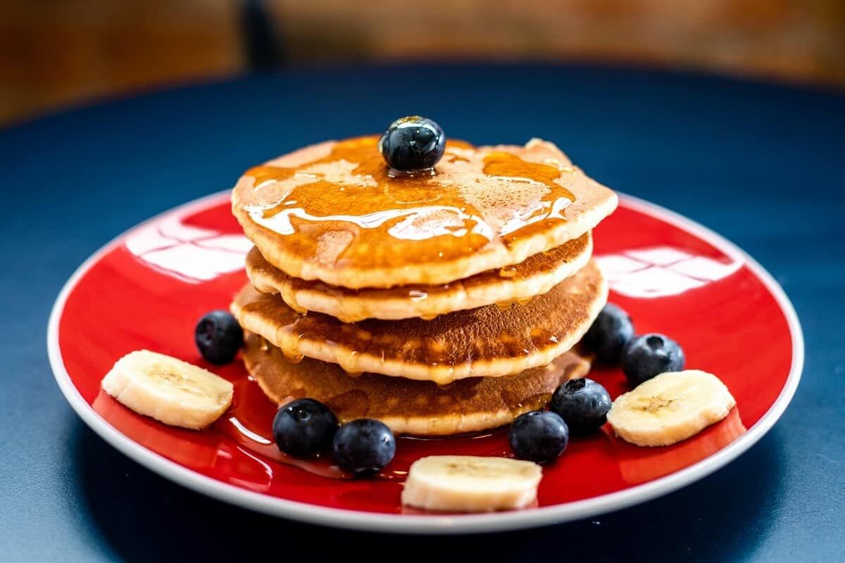 Pancakes with maple syrup drizzled on top with blueberries and banana slices on the plate