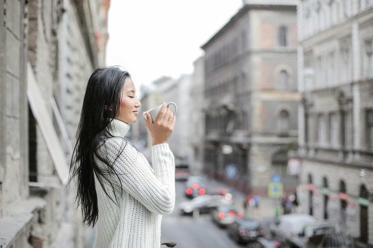 Lady standing outside, drinking coffee.