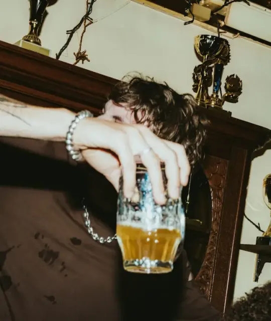 Young person resting on a mantelpiece holding a pint of beer